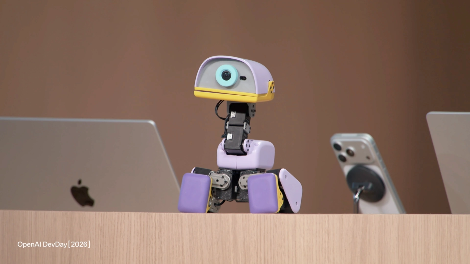 Lavender, the small purple robot used in the DevDay demonstration, sits between laptops on the presentation desk.